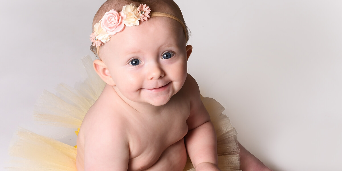 Glad bebis med blommigt pannband och tyllkjol i fotostudio