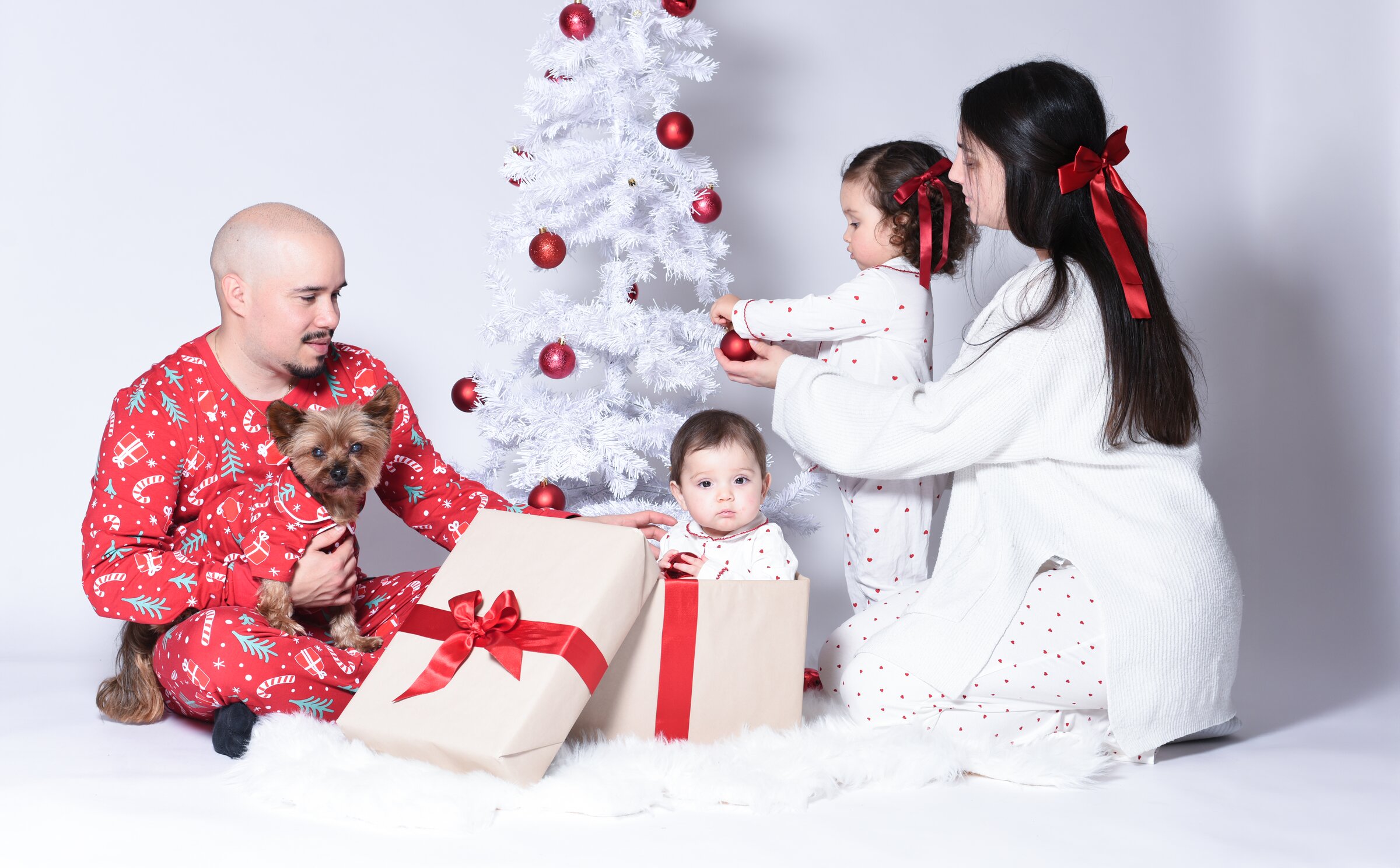 Familj i röda jul-pyjamas med hund och julklappar vid julgran