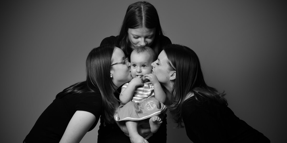 Svartvit bild på syskon som håller sin yngsta tätt - familjefotografering